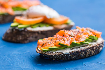 Sandwiches with smoked salmon, eggs, sauce and avocado on blue background. Concept of breakfast and healthy nutrition.