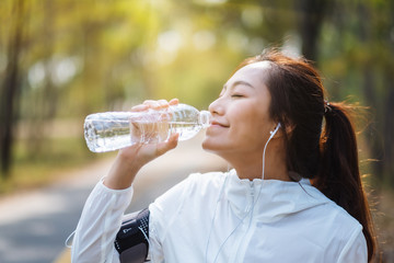 Closeup image of an asian female runner drinking water from bottle after jogging in city park