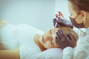 Young woman undergoing procedure of eyebrow permanent makeup in beauty salon