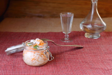 Jar of sauerkraut on the background of a glass of vodka and decanter. Sauerkraut in glass jar as a snack for vodka.