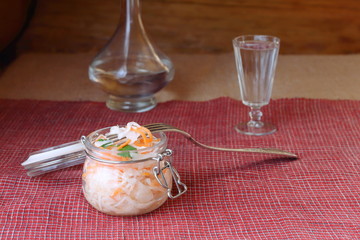 Jar of sauerkraut on the background of a glass of vodka and decanter. Sauerkraut in glass jar as a snack for vodka.