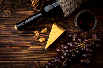 Obraz premium Red wine, grape, cheese and walnut on dark wooden background.