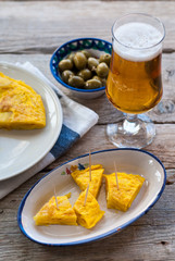 Tortilla de patatas con copa de cerveza y bol con aceitunas sobre mesa vieja de madera