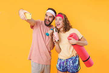 Portrait of athletic couple taking selfie with dumbbells and fitness mat