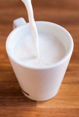 Taza llenándose de leche con un chorro sobre tabla de madera