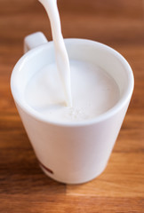 Taza llenándose de leche con un chorro sobre tabla de madera