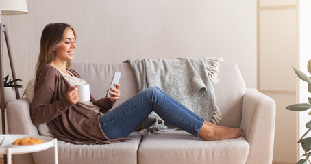 Fototapeta premium Young woman enjoying coffee and web surfing on smartphone