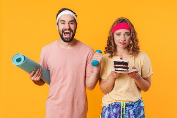 Portrait of man holding mat and dumbbell while woman holding cake