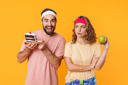 Portrait of athletic young couple choosing beetwen cake and apple