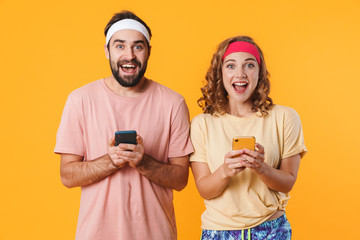 Portrait of athletic young couple smiling and using cellphones together