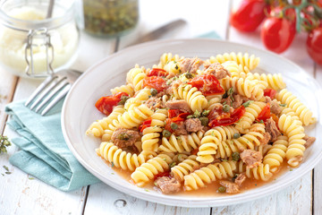 Delicious Italian pasta fusilli in fresh cherry tomato, tuna and capers sauce with grated parmesan cheese at the background on white rustic wooden table