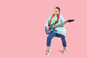 Young guitarist woman in oversize clothes with electric guitar with copyspace isolated on pink background