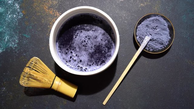Matcha blue tea powder and matcha tea in white bowl, bamboo tusaku on blue board.