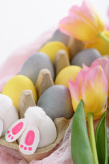 Fototapeta na wymiar close-up of pastel Easter eggs with pink tulips, Easter Bunny on pink fabric on white background
