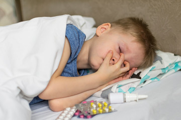 Obraz na płótnie Canvas A sick child with a fever and a headache lies in bed. The child sleeps around drugs and pills. Flu colds disease virus bacterium.