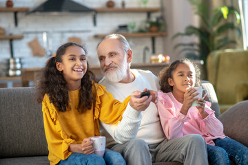 Two dark-skinned girls and their granddad watching tv together