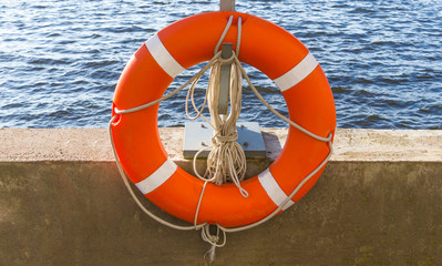Orange lifebuoy and old rope hanging by the river