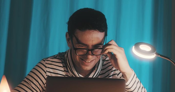 Close-up portrait caucasian business man with eye glasses smiling and using computer in home workspace. 4K slow motion.