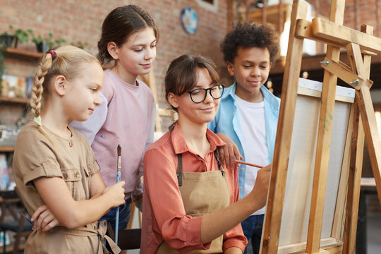 Young woman painting on easel and group of children watching for the process at art studio