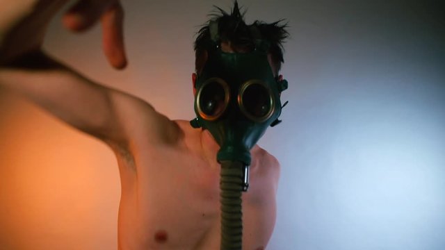 A man dances on the rave of electronic music. A gas mask is put on his head. Makes dance movements with his hands.