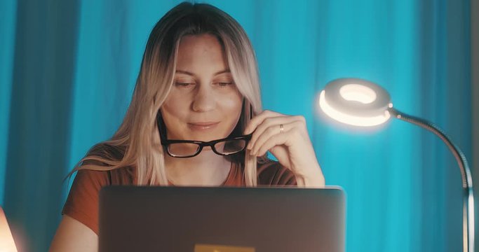 Close-up portrait caucasian business woman with eye glasses smiling and using computer in home workspace. 4K slow motion.