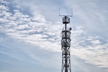 Close-up of lattice mast with base station for mobile communications against blue sky with clouds. Seen in Germany in February