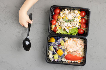 girl holds spoon to eat school lunch into food containers, raw vegetables for health, top view