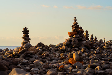 Balanced stone pyramide on shore of the ocean at dawn. Sea pebbles tower closeup symbolizing stability, zen, harmony, balance.