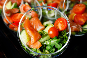 Top of buffet table with glass cups with salad of red fish, tomatoes, cucumber, herbs
