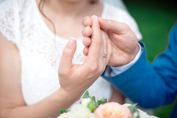 Hands of the newlyweds bride and groom with gold wedding rings close-up on a background of a wedding bouquet of roses.