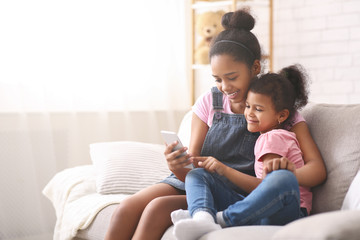 Fototapeta premium African american sisters watching cartoons on mobile phone