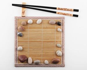 Chopsticks are located on a stand next to a bamboo mat with stones