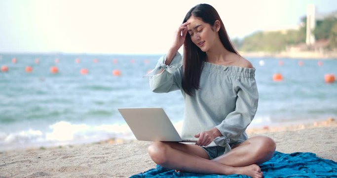 Woman freelancer works on the beach. Young asian female working with computer laptop on the tropical island beach with happy emotion. Technology for wherever concept.