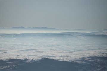 Beautiful view of the mountain range partially covered by fog and snow with clear blue sky.