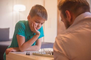 young man and son playing chess together. Son is thinging about his next move.