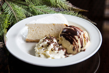 A slice of cheese cake with ice cream and whipped cream on a white plate. Conceptual food photography with plant decoration.