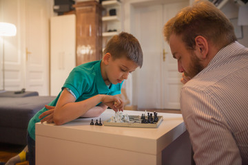 Fototapeta premium Son is moving a figure on the chess board against his father.
