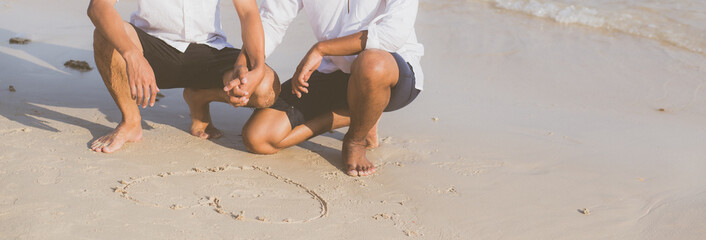 Young asian couple gay romantic drawing heart shape together on sand in vacation, homosexual happy and fun with love sitting on sand at the beach in travel summer, LGBT legal concept, banner website.