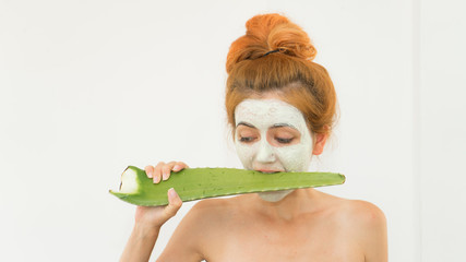 Red haired woman with cosmetic face clay mask on his face wearing  towel after bath and holding...