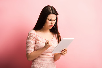 angry girl showing clenched fist during video chat on digital tablet on pink background