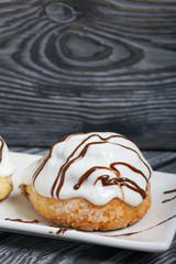 Cinnabons in white glaze, decorated with chocolate. Lie on a plate. Against the background of brushed pine boards.