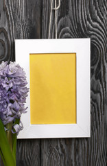 Lilac blooming hyacinth. The photo frame is white with a yellow field. Located against the backdrop of brushed pine boards painted in black and white.