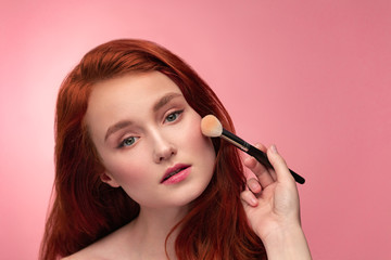 Makeup artist applies powder. Hand of make-up master, painting cheeks of young redhead girl....
