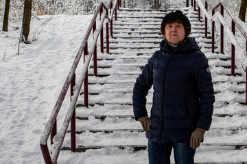 Winter. A lady in a hat, a blue sports jacket is standing in front of a staircase in a snowy forest.