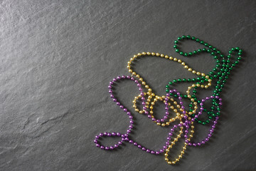 Purple, green and gold Mardi Gras beads on a gray slate table with copy space