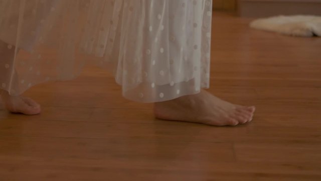 A young woman walks barefoot on the parquet in a sunny room. Slow motion.