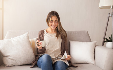 Smiling woman sitting on couch and reading magazine