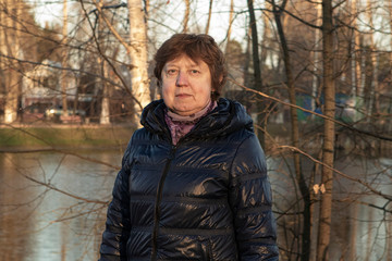 Fototapeta na wymiar Woman in a blue jacket with a scarf around her neck against the backdrop of a city pond
