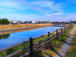 早春の土手の小道のある放水路風景