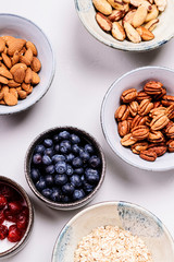 Ingredients for homemade granola: oatmeal, dried cherry, pecans, almond, brazilan nuts, blueberries in a bowls on light background. Healthy diet breakfast. Flatlay. Top view. Selective focus